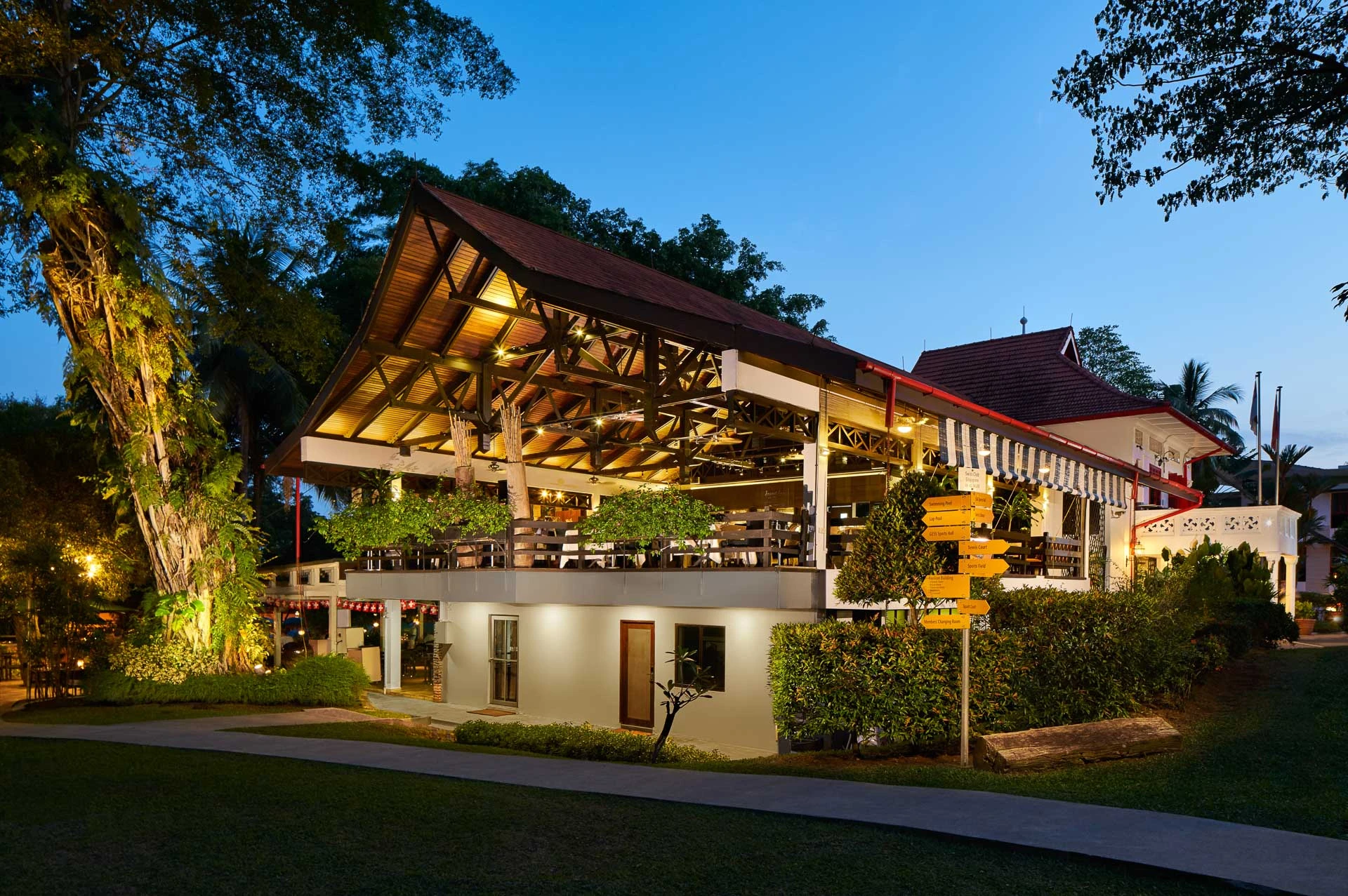 Swiss Club Singapore Arbenz restaurant exterior at dusk with timber roof structure and garden pathway