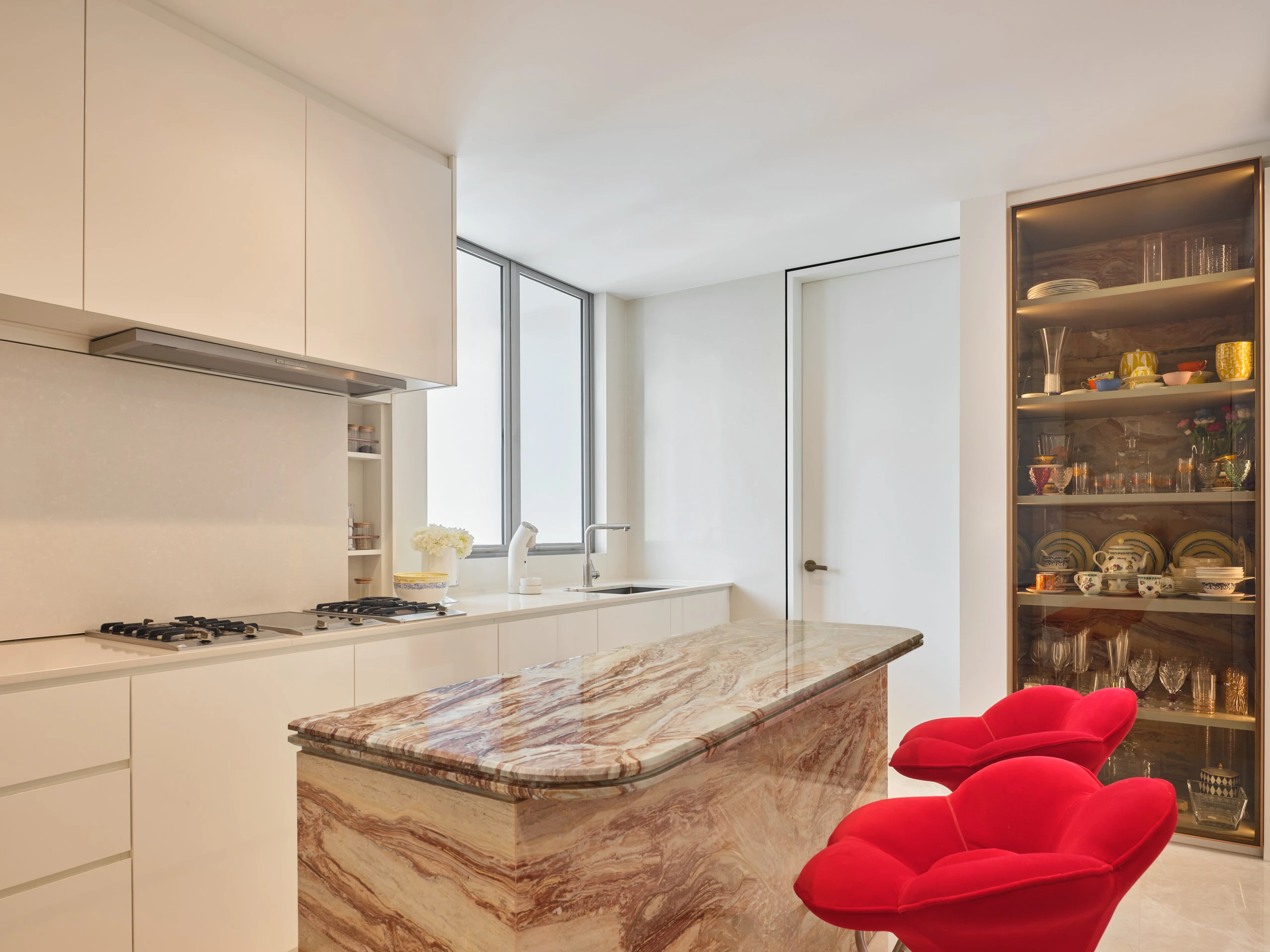 Modern kitchen with marble countertops, sleek cabinetry and red accent chair