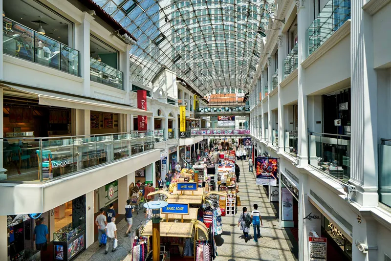 Daytime view inside a glass-roofed multi-level shopping arcade with market stalls
