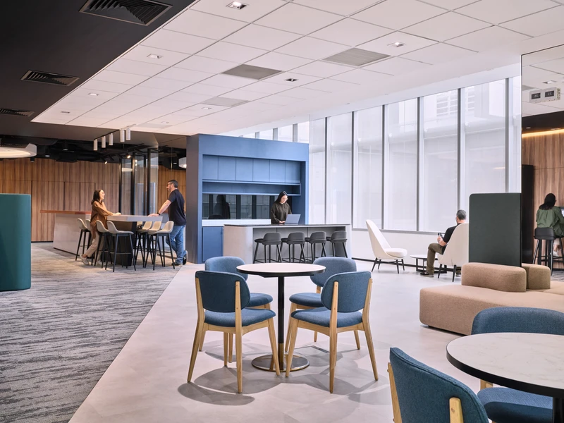Modern office lounge with blue chairs, high tables and people working casually
