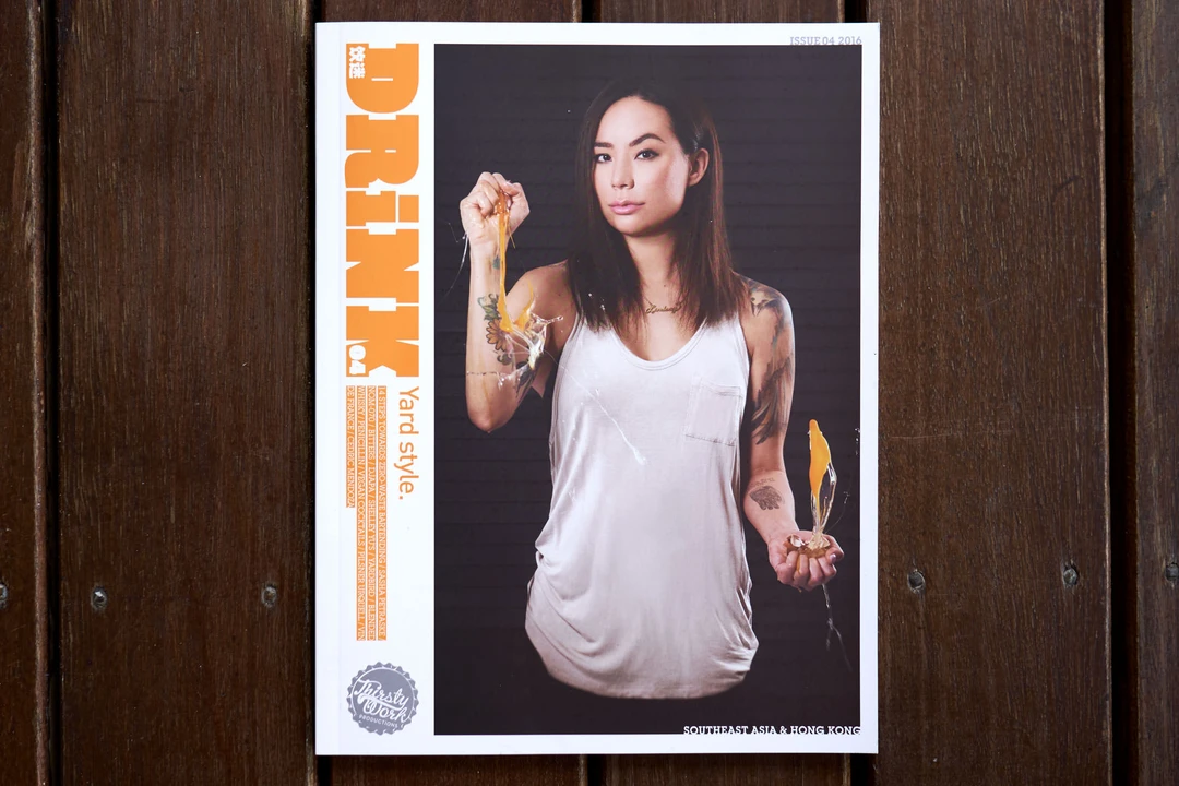 Drink Magazine issue 04 cover on dark wood planks, showing a woman in a white tank top holding cocktail ingredients, with orange masthead.