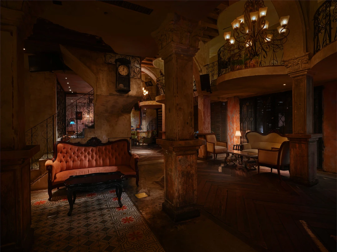 Double-height salon with iron chandelier, mezzanine balcony and tufted sofas — Havana Social Bangkok restaurant photography
