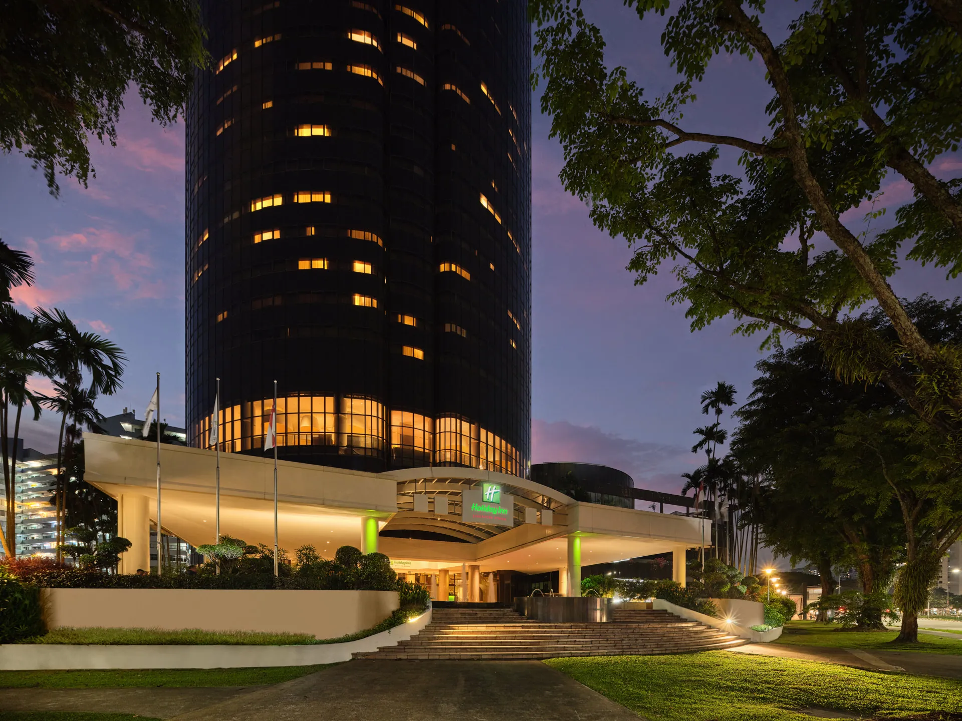 Hotel tower with glowing windows and illuminated entrance at twilight — Holiday Inn Atrium Singapore architectural photography