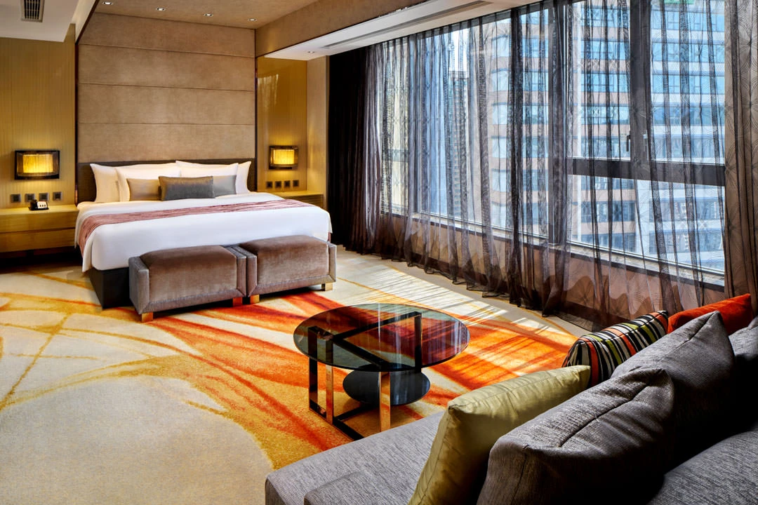 Suite bedroom with taupe headboard, velvet bench and orange abstract rug — Crowne Plaza Hong Kong hospitality photography