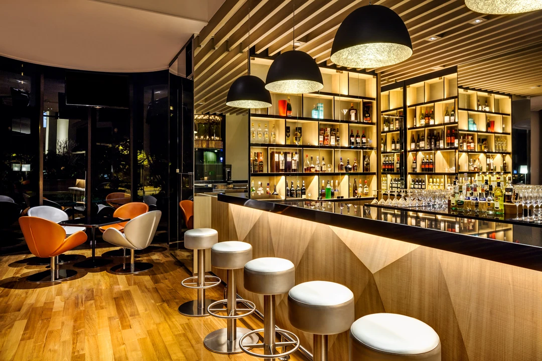Hotel bar with backlit spirit shelving, gold dome pendants and leather chairs