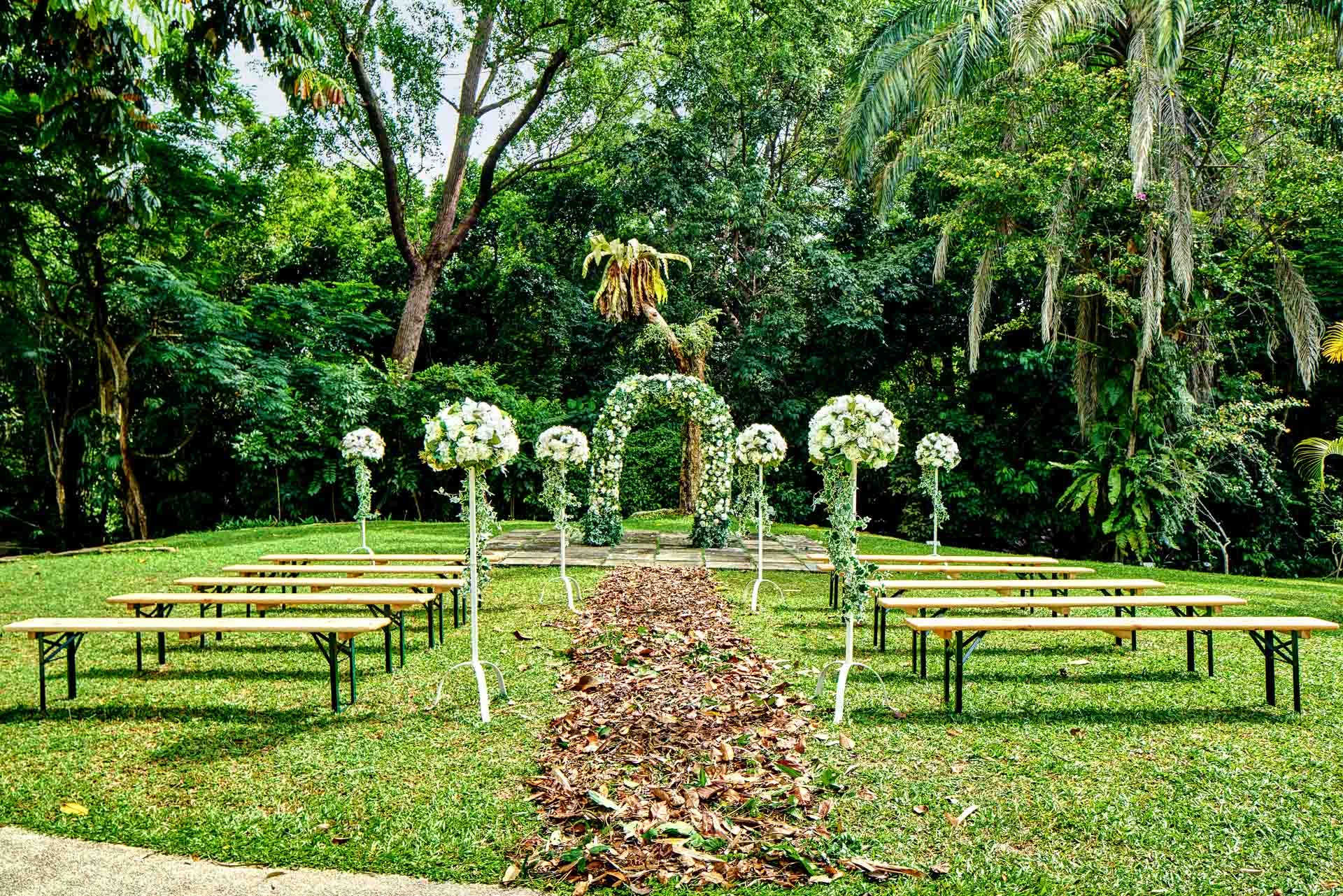 Garden wedding with white floral arch and wooden bench seating