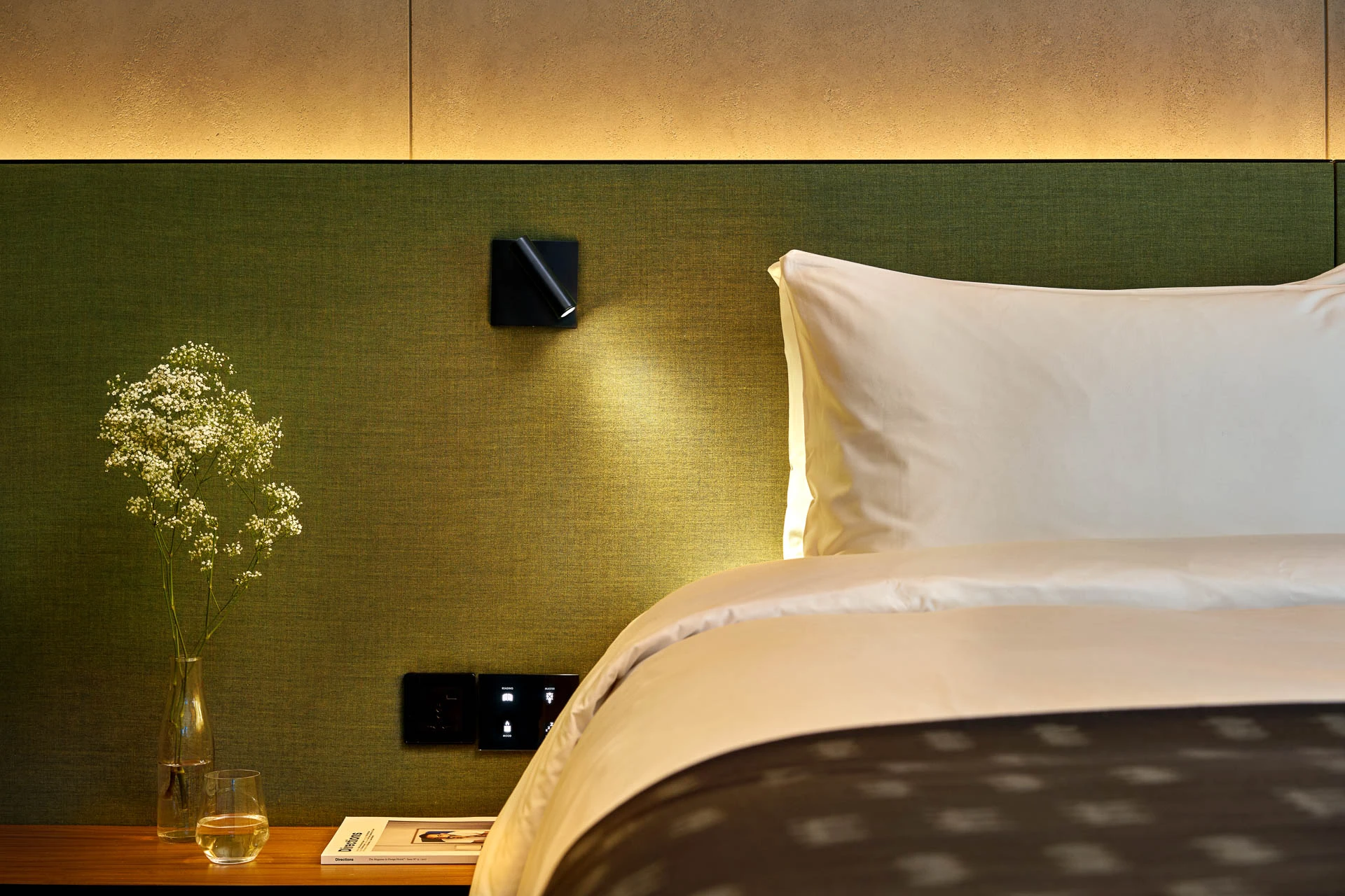 Bedside detail with green headboard, black reading light and cove lighting