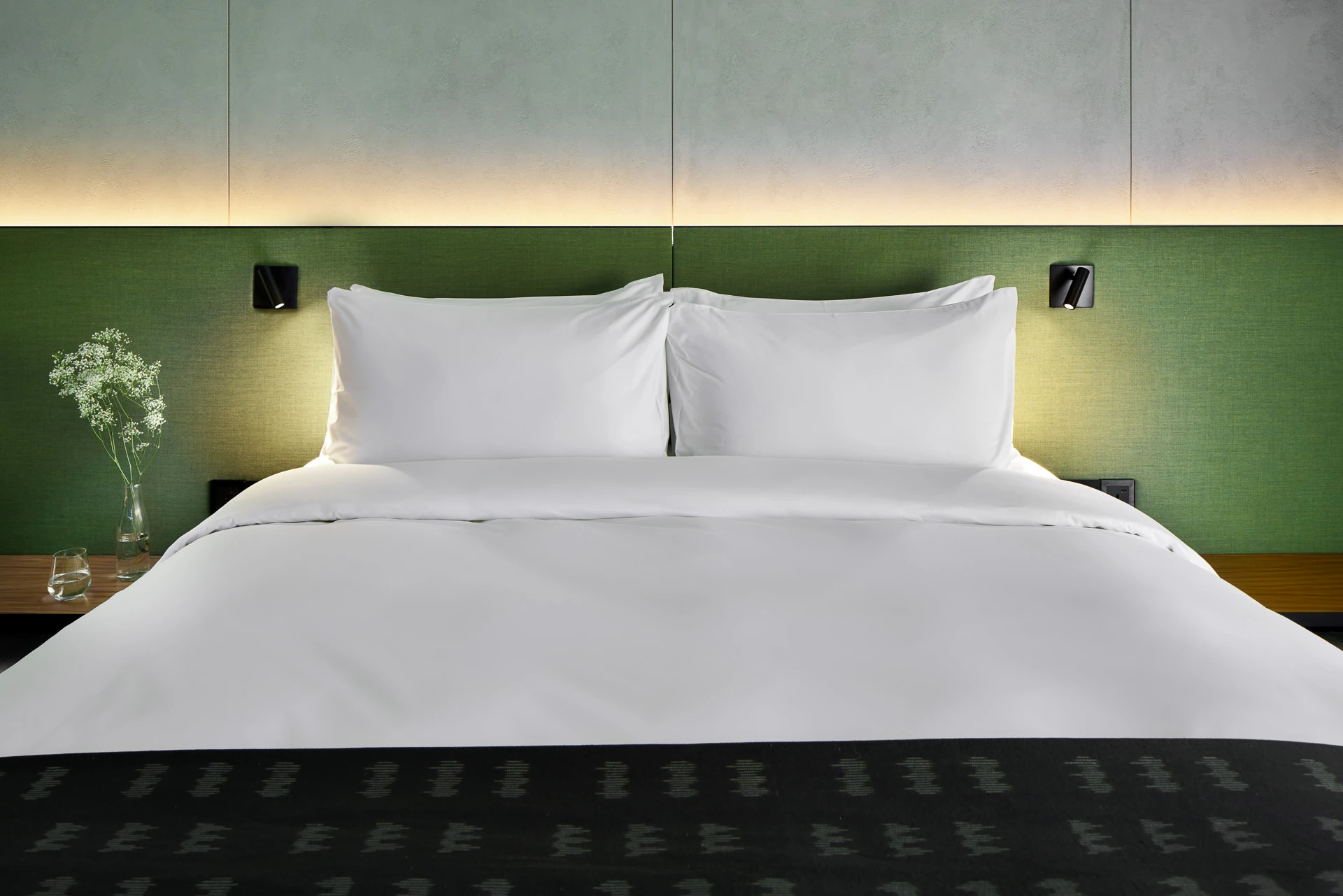 King bed with olive headboard, black wall sconces and LED halo