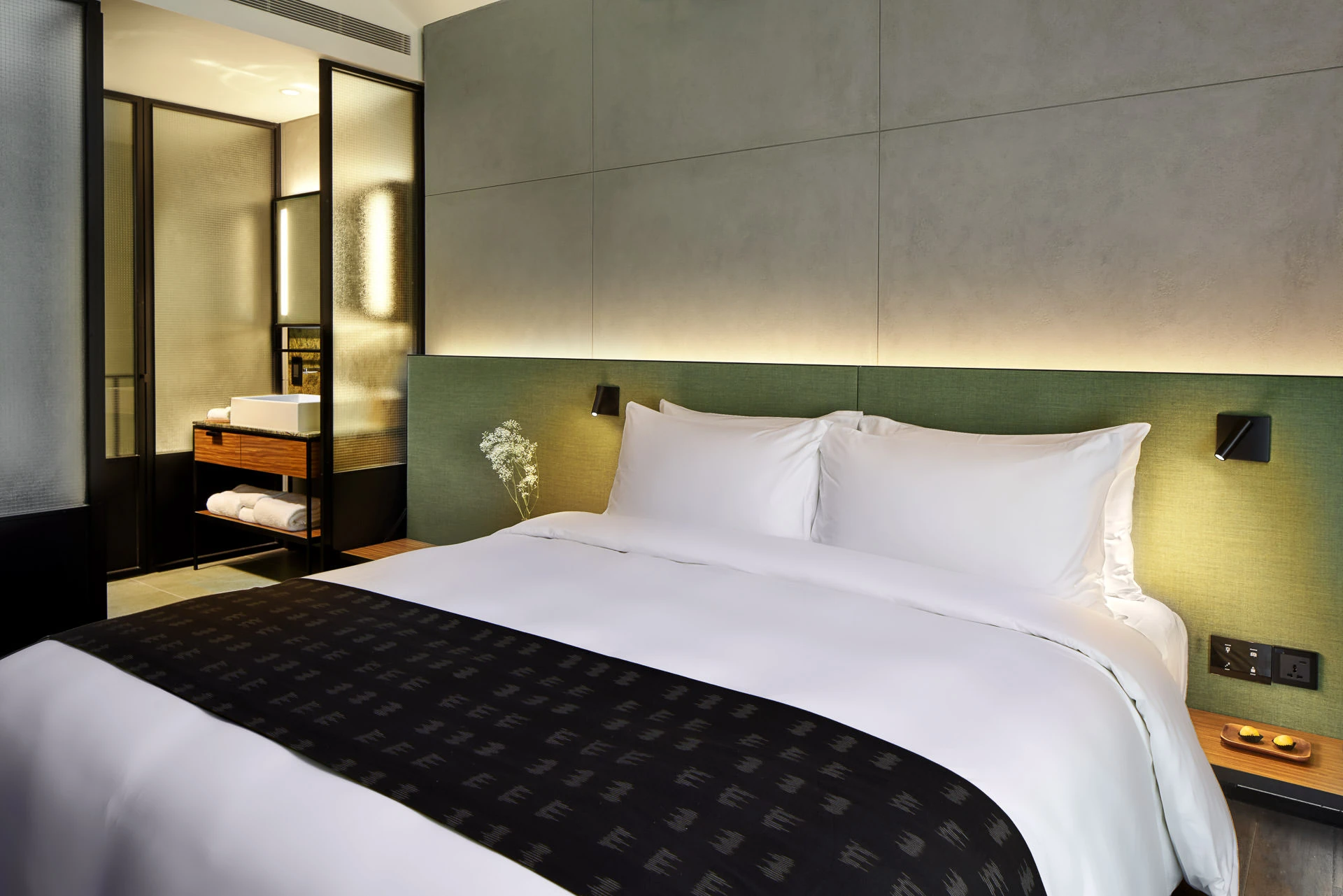 Room with green headboard, glass bathroom partition and cove lighting zones