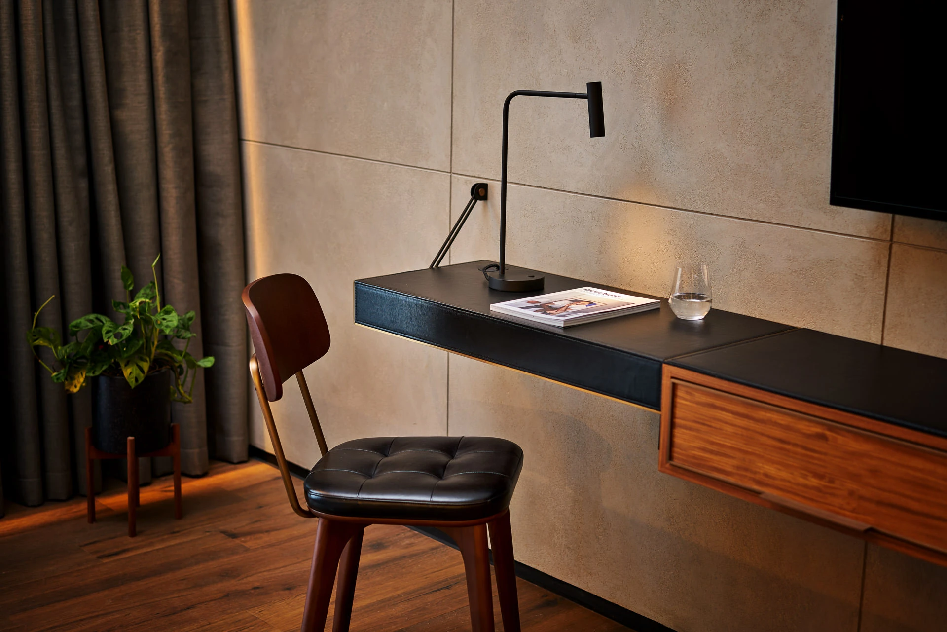 Angular desk lamp on leather-topped walnut console against concrete wall