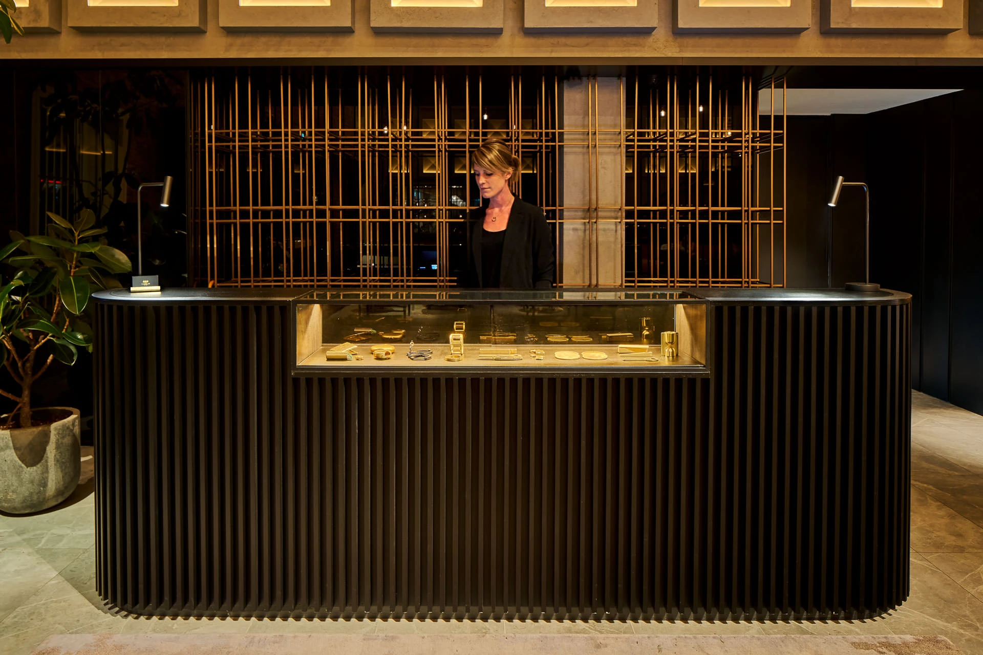 Concierge at reception with copper lattice backdrop and gallery lighting