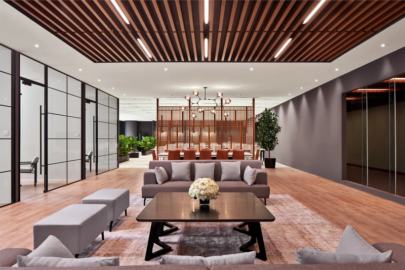 Spacious office lounge with wood-slat ceiling, grey sofas, wooden screen and plants