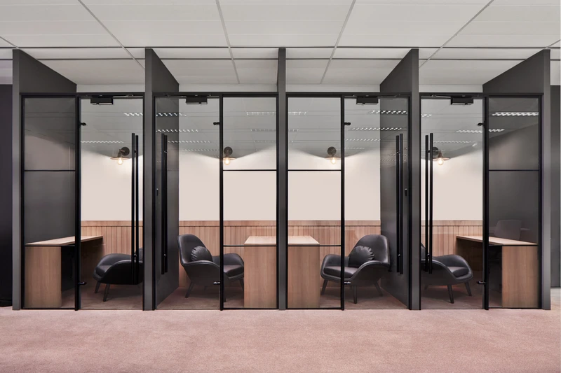 Row of glass-enclosed private meeting pods with black leather chairs and wood desks