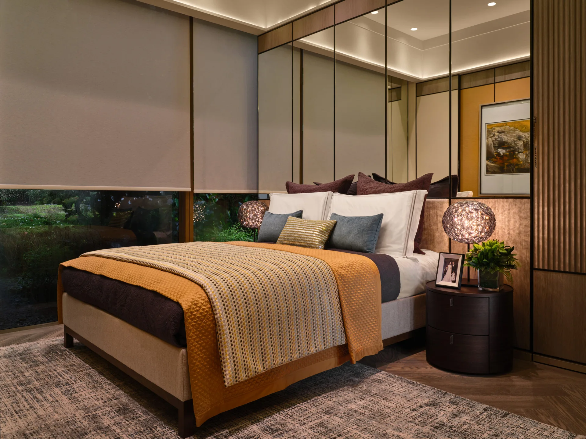 Showflat bedroom with mustard quilted throw, mirrored wall panels, pendant lamp and garden views