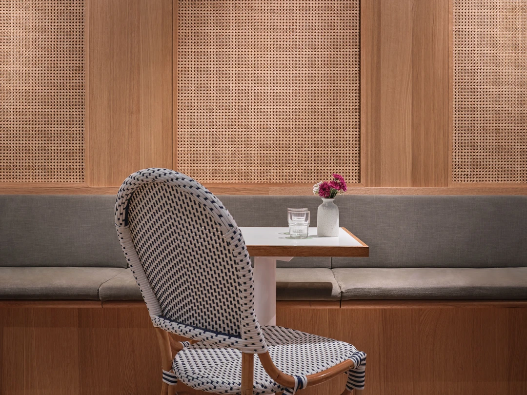 Woven chairs and wooden table detail with greenery backdrop