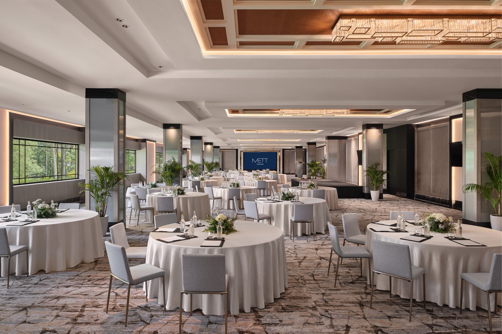 METT Singapore Grand Ballroom viewed from the side with cluster banquet tables, stage screen, coffered ceiling lights, and event seating