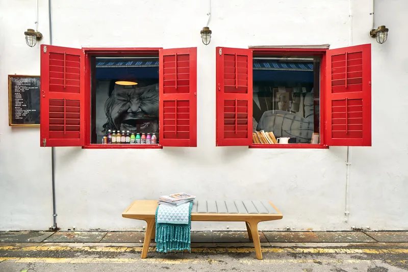 Wooden bench with a teal throw beneath red-shuttered windows on a white wall