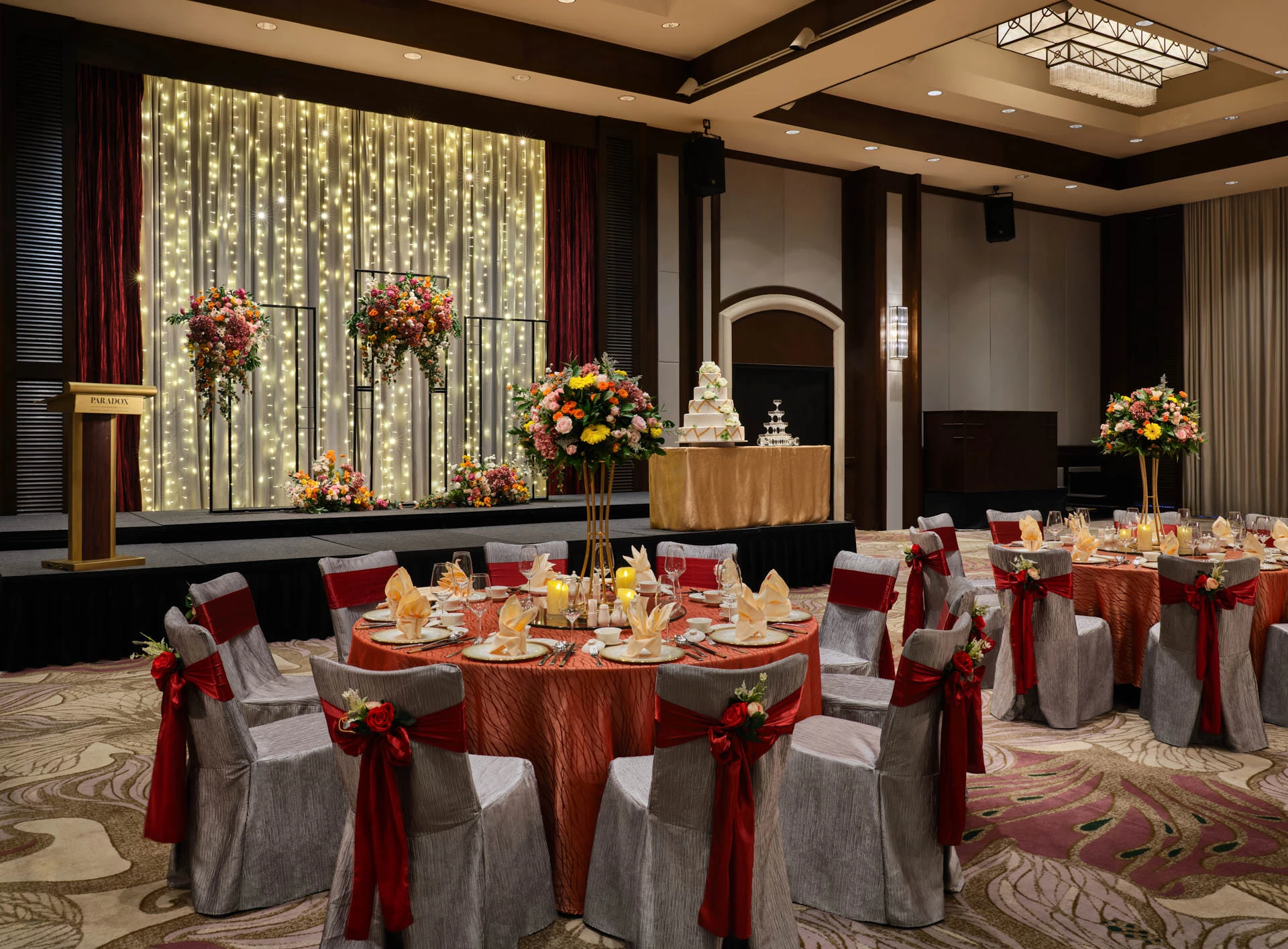 Paradox Singapore Blissfully Peach wedding reception with red and gold decor, tiered cake, and floral stands