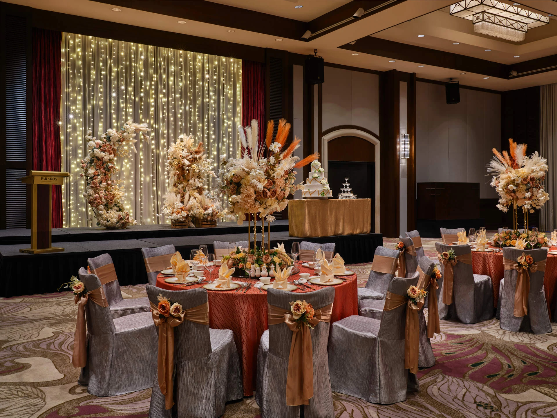 Paradox Singapore ballroom wedding setup with burnt-orange linens, dried roses, and gold accents