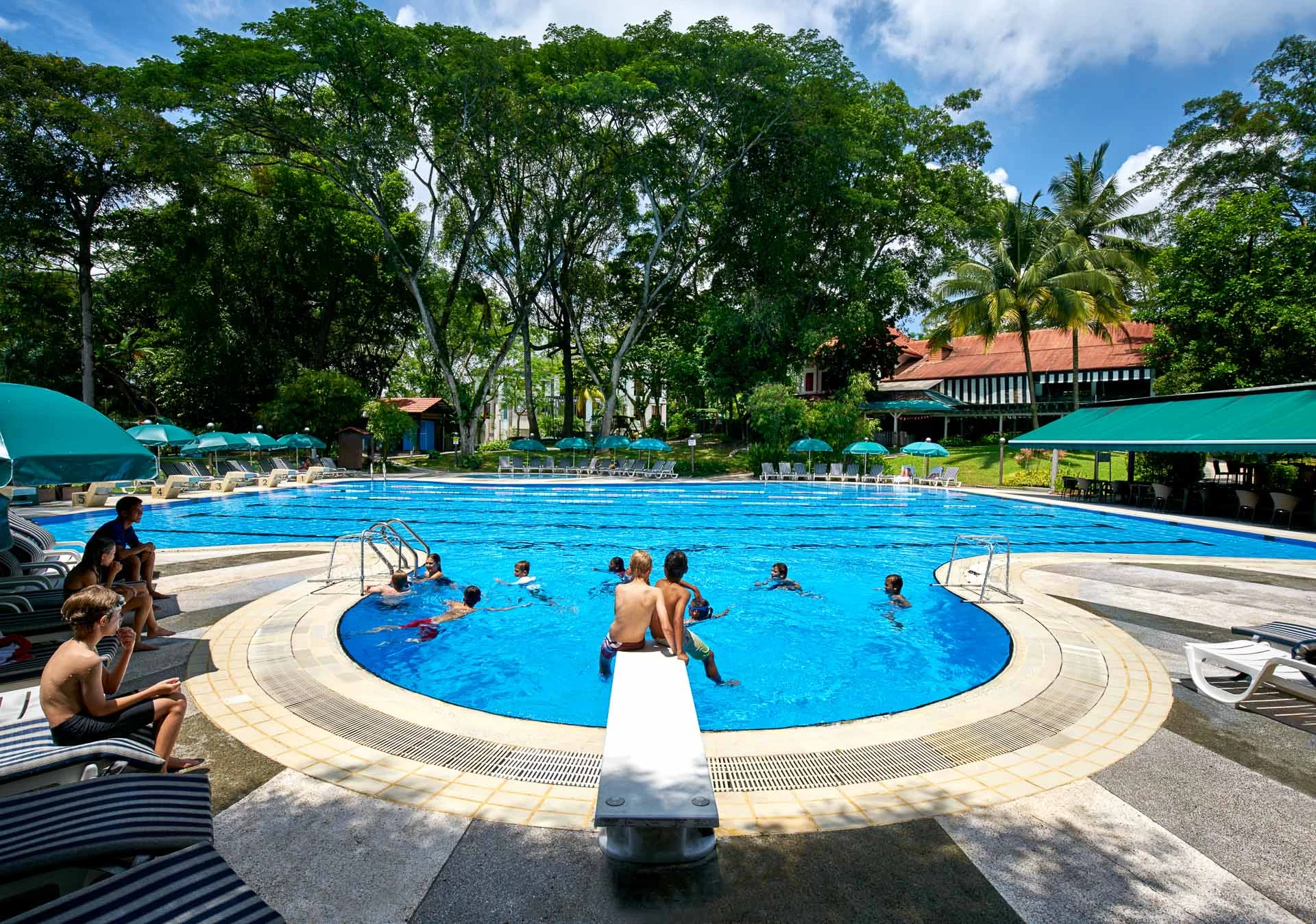 Children swimming in outdoor pool with loungers and pavilion