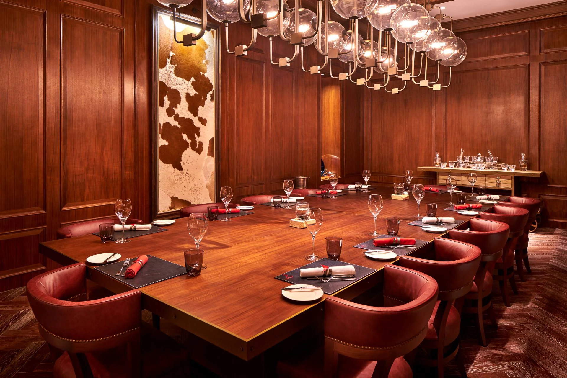 Private dining with red barrel chairs, cowhide art and globe chandelier
