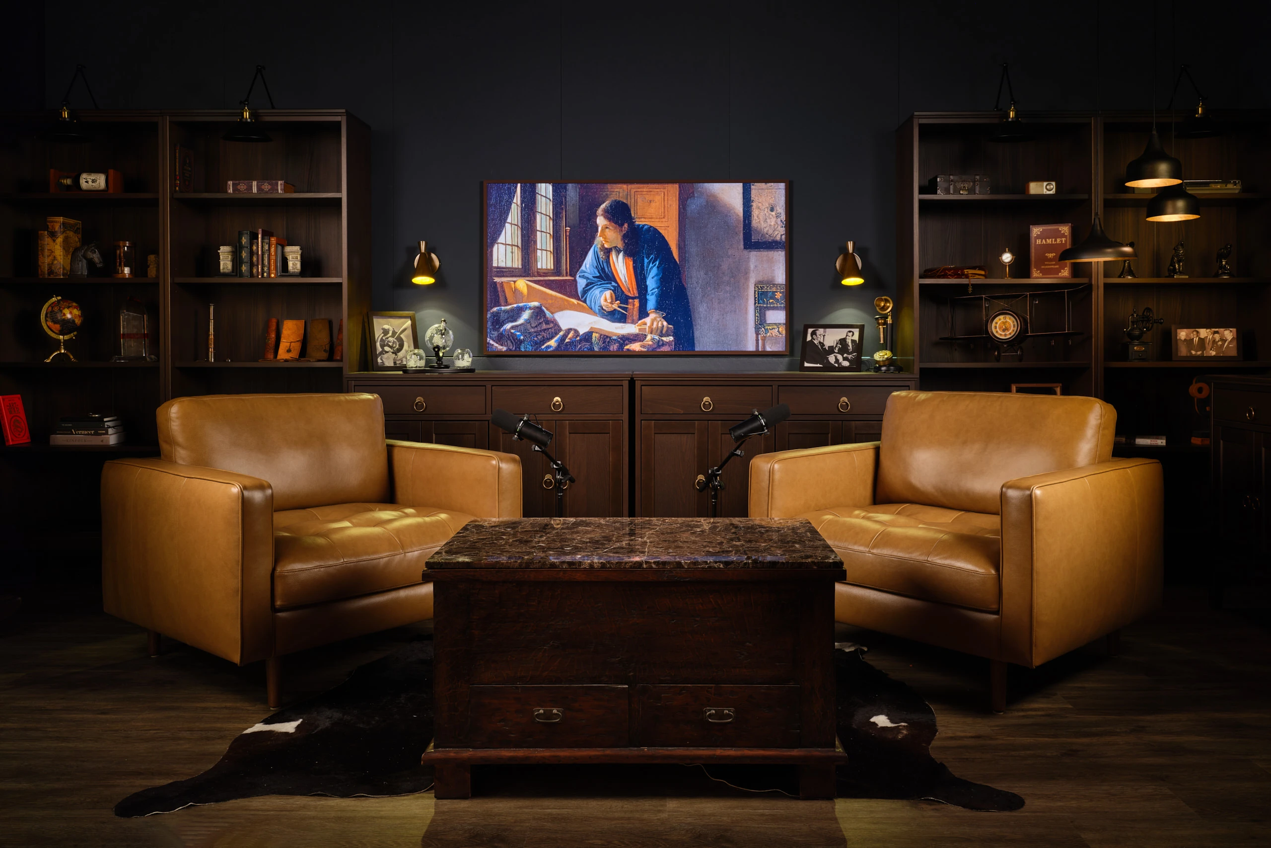 Dark library podcast studio with cognac leather chairs, bookshelves and Vermeer art