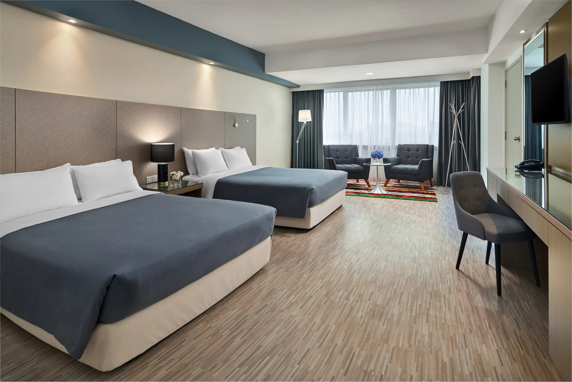 Deluxe twin suite with tufted armchairs on colourful rug and floor lamp — RELC Hotel Singapore interior photography