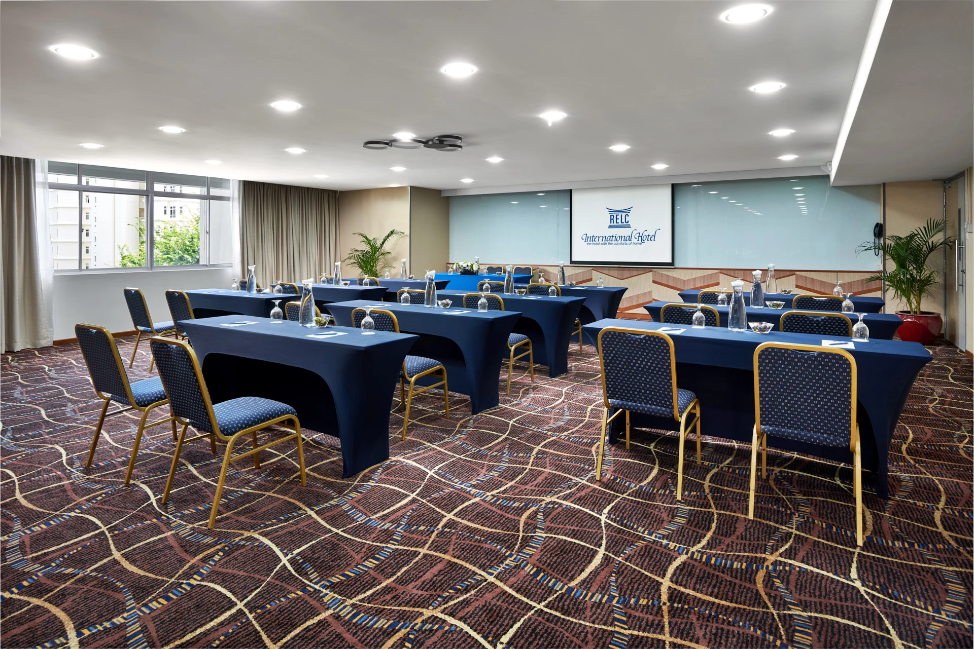 Classroom meeting with branded screen, potted palms and blue chairs — RELC Hotel Singapore meeting room photography