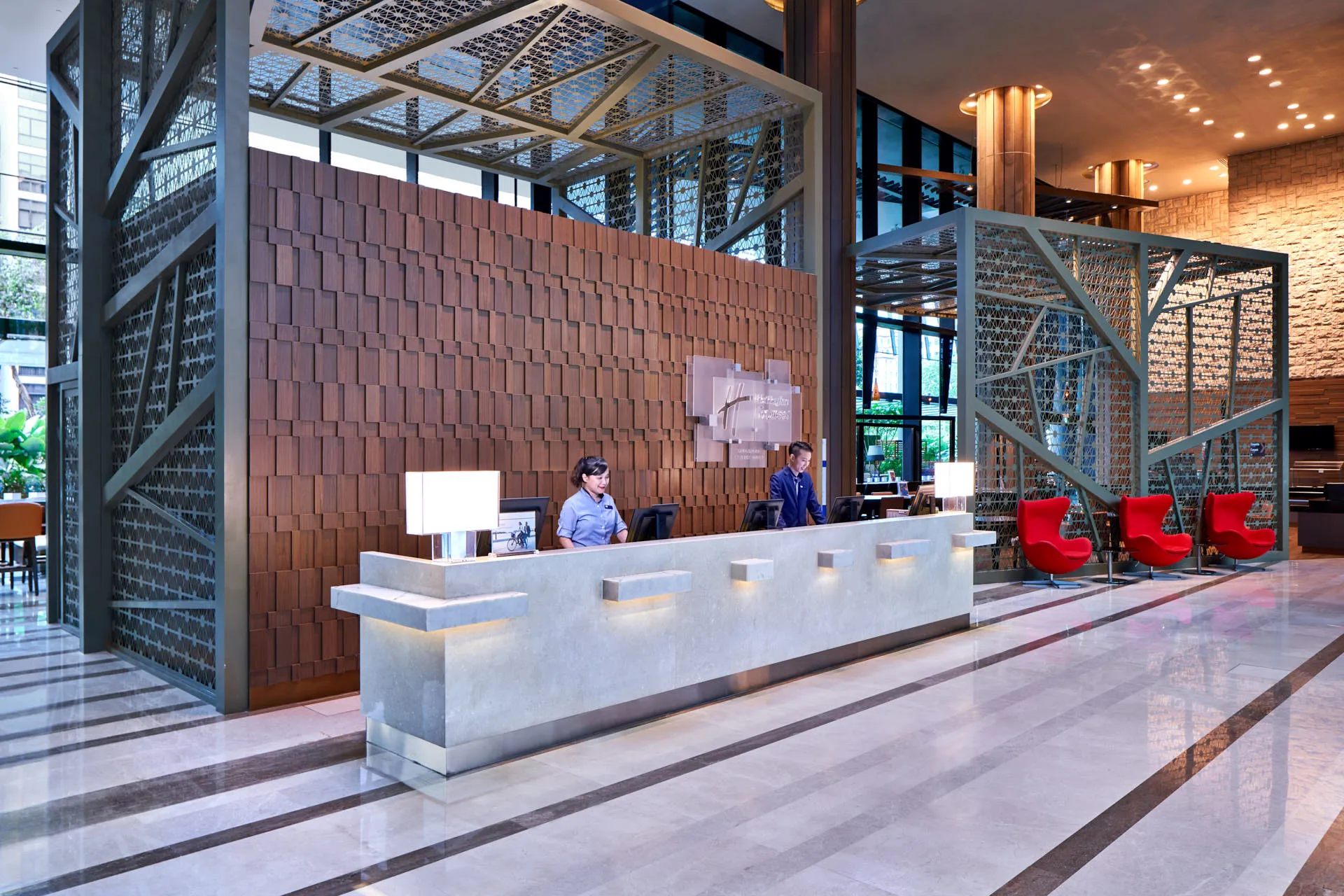 Hotel lobby with stone reception desk, metal lattice screens and red egg chairs — Holiday Inn Express Clark Quay interior photography