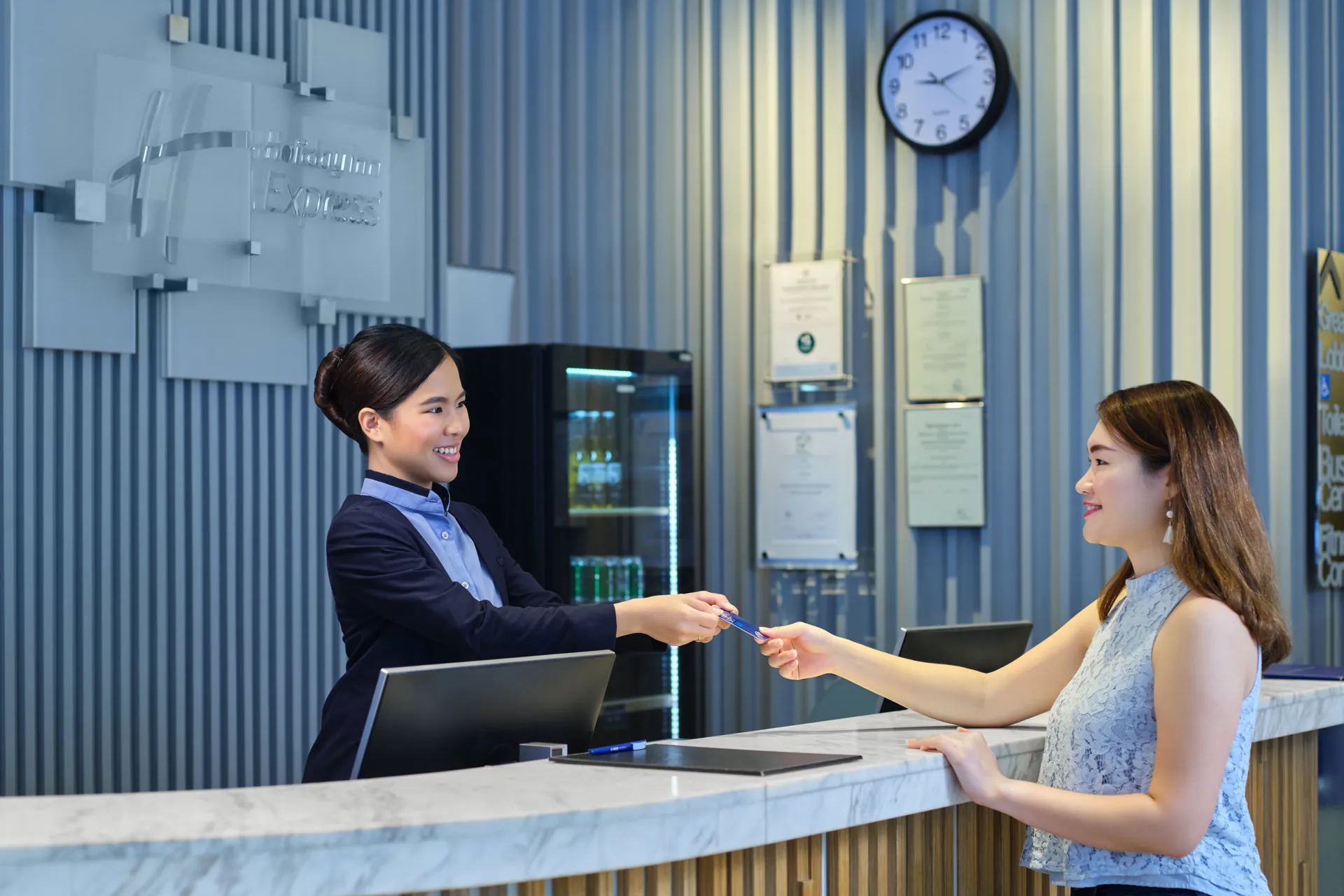 Staff member handing key card to guest at reception desk — Holiday Inn Express Orchard hospitality photography