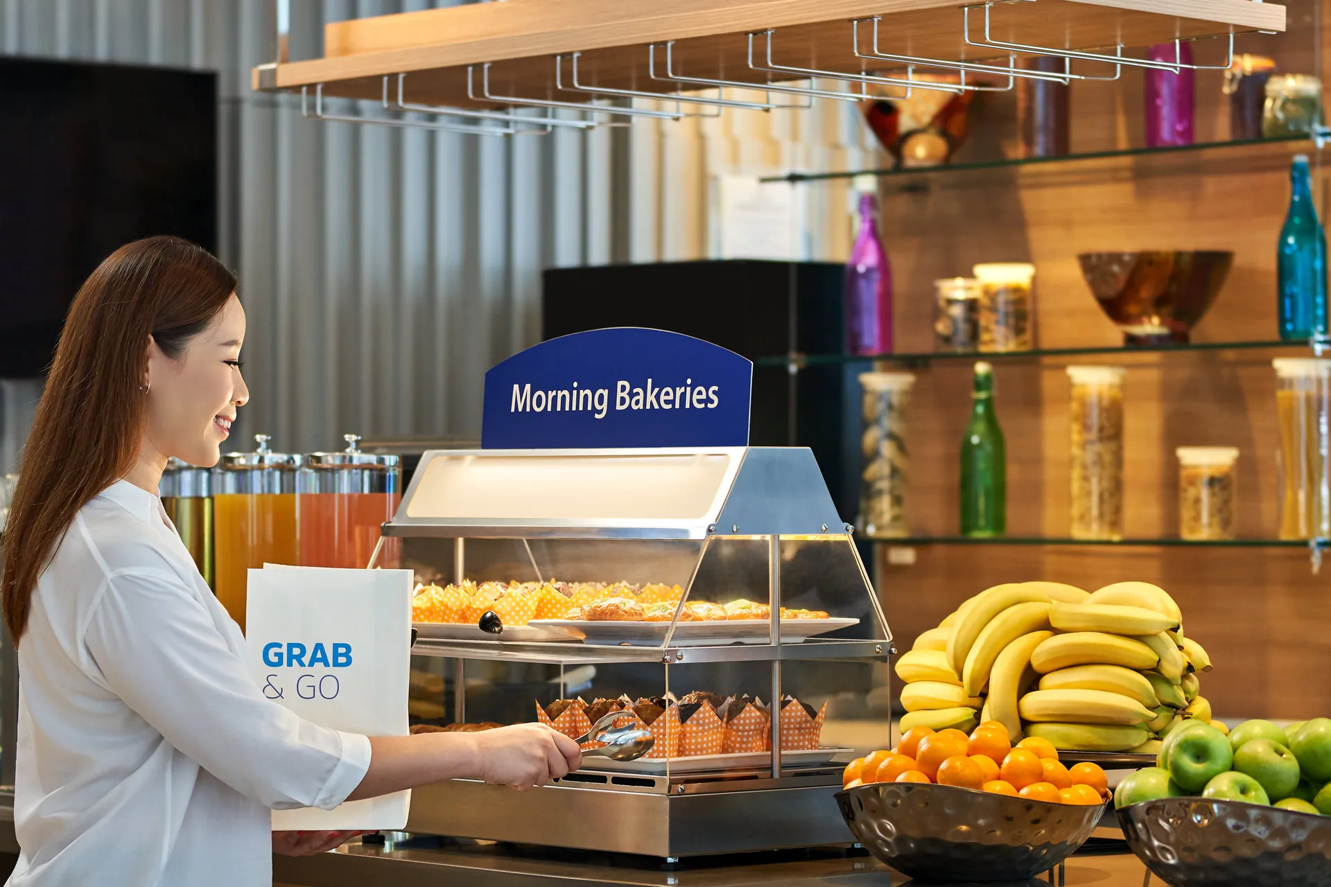 Guest selecting from grab-and-go breakfast display with fresh fruit — Holiday Inn Express Orchard hospitality photography