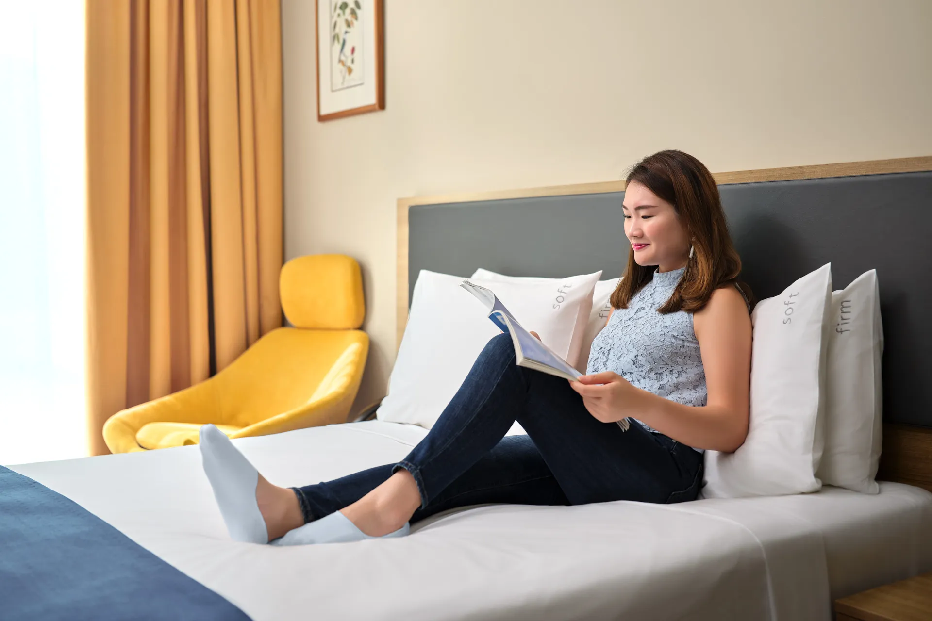 Woman reading magazine on king bed with golden curtains — Holiday Inn Express Orchard hotel lifestyle photography
