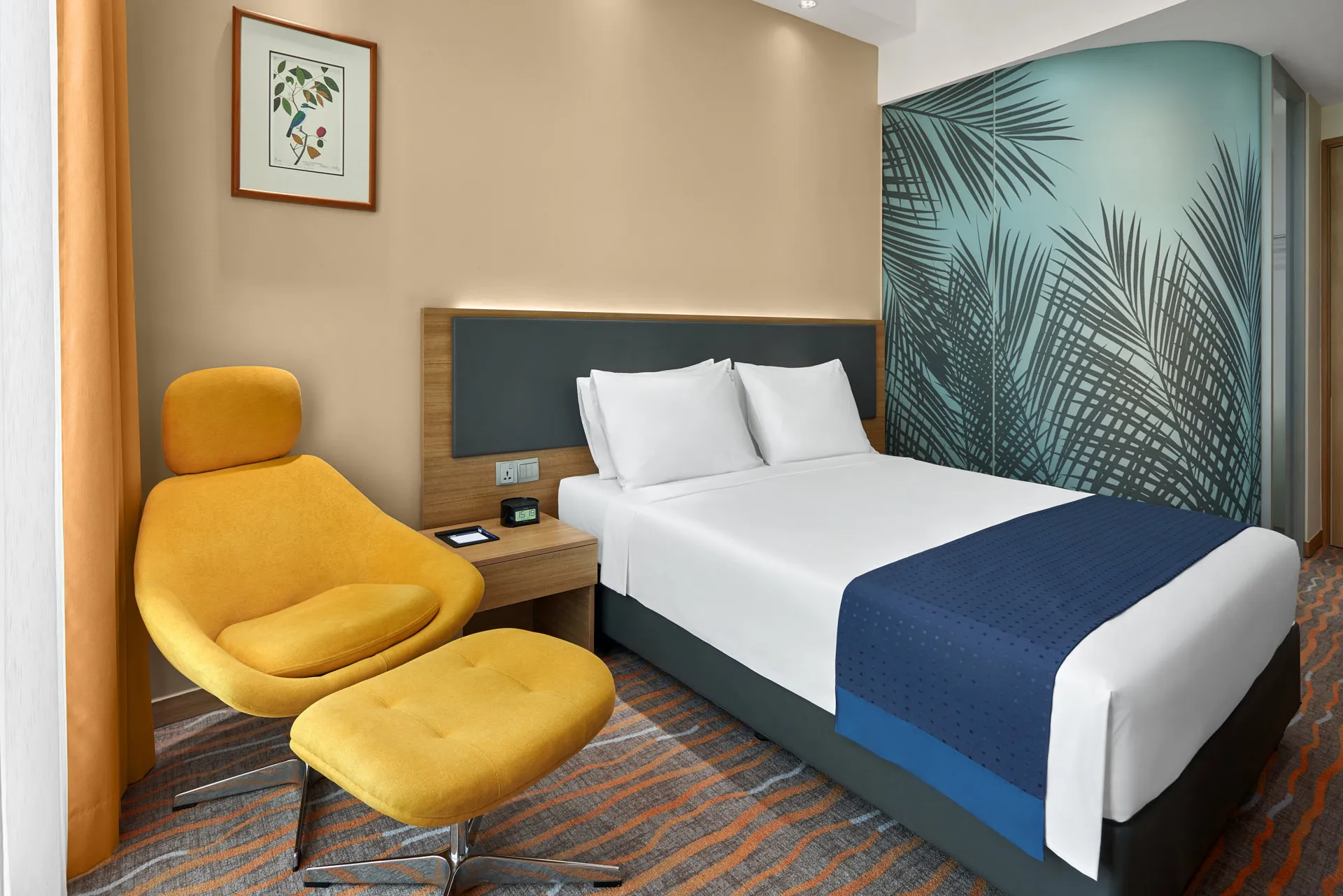 Queen room with mustard lounge chair and tropical accent wall — Holiday Inn Express Orchard interior photography