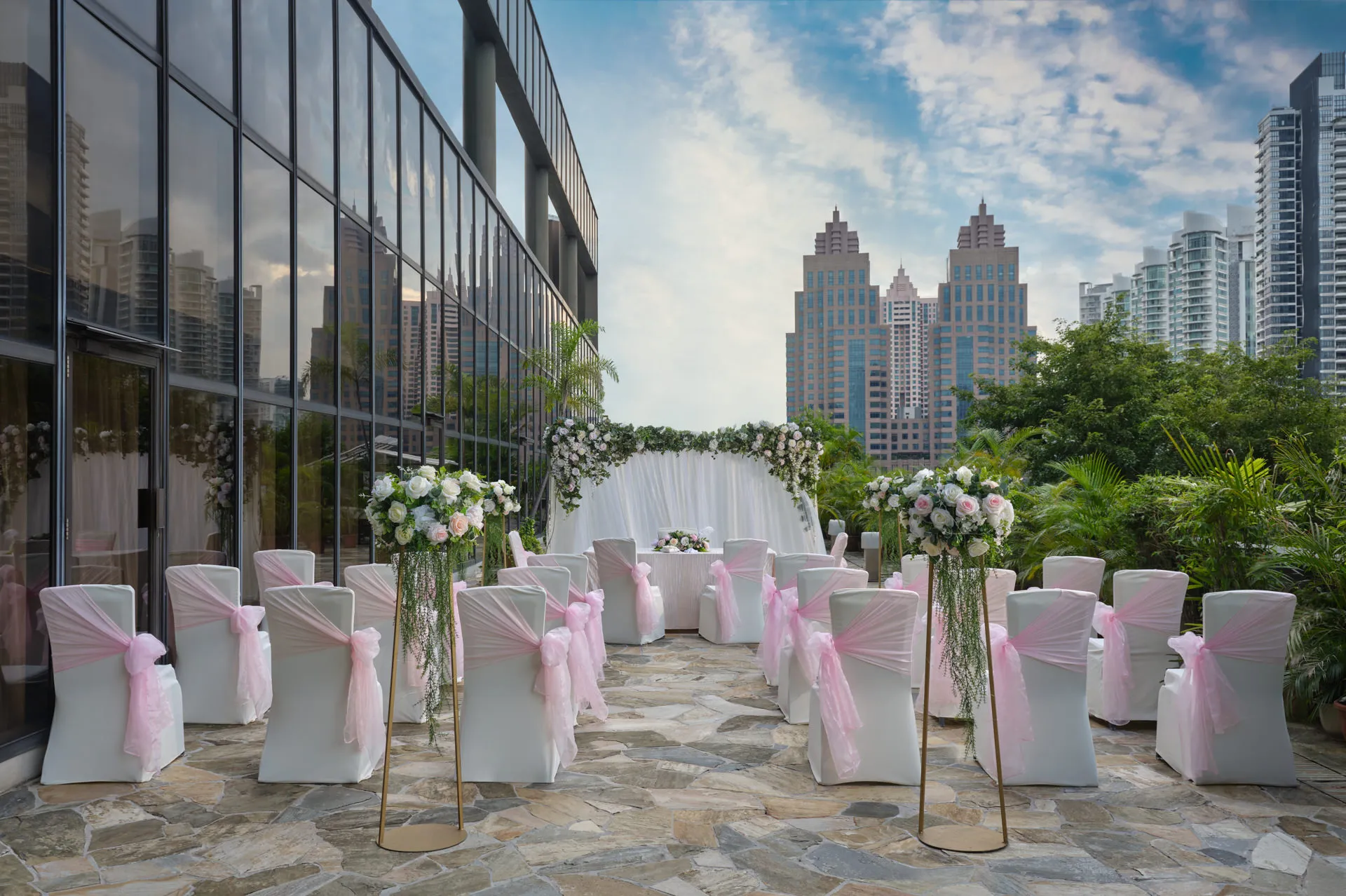 Rooftop wedding ceremony with floral arch and white chairs overlooking Singapore skyline — Holiday Inn Atrium hospitality photography