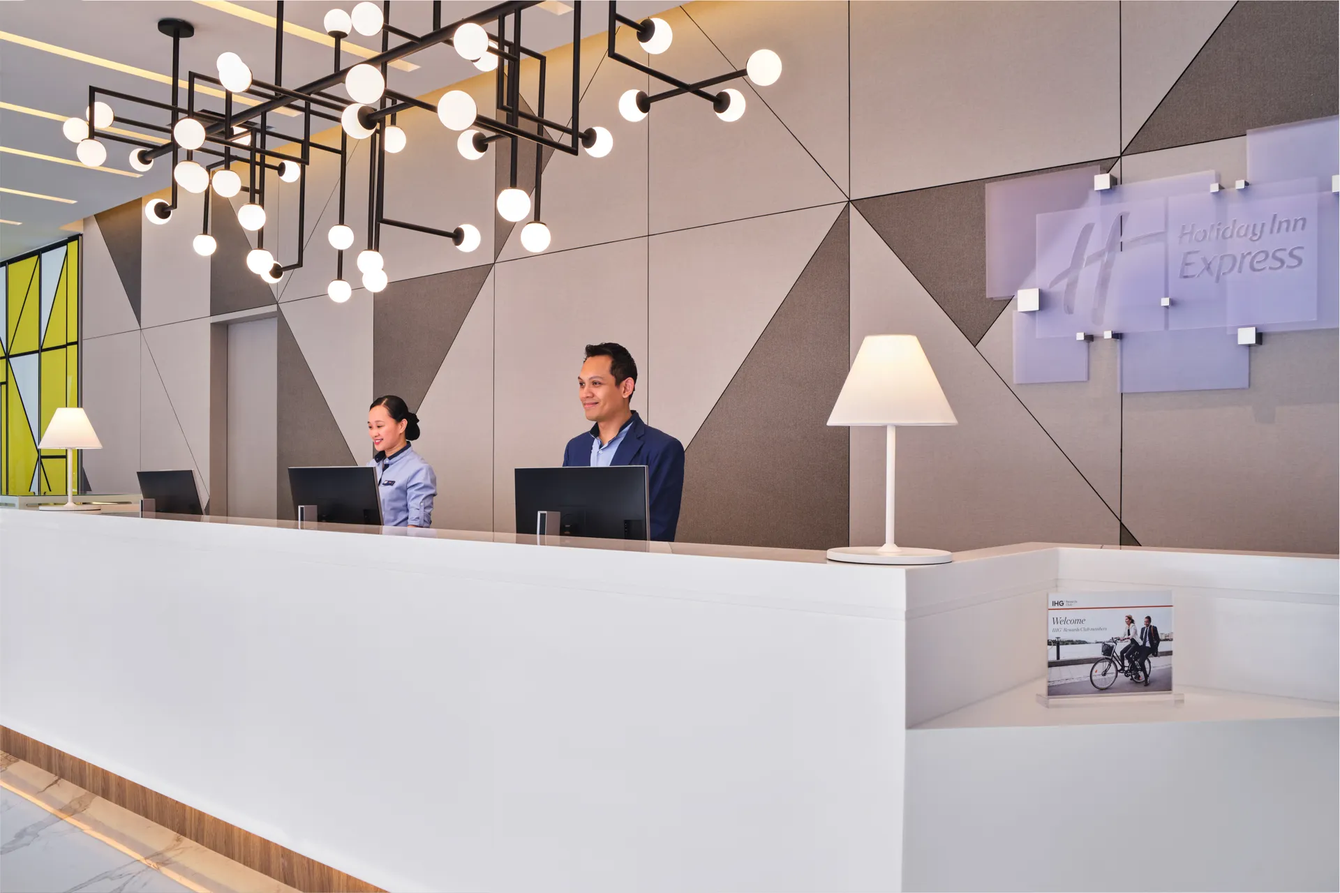 Front desk with globe chandeliers and smiling staff — Holiday Inn Express Serangoon hospitality photography