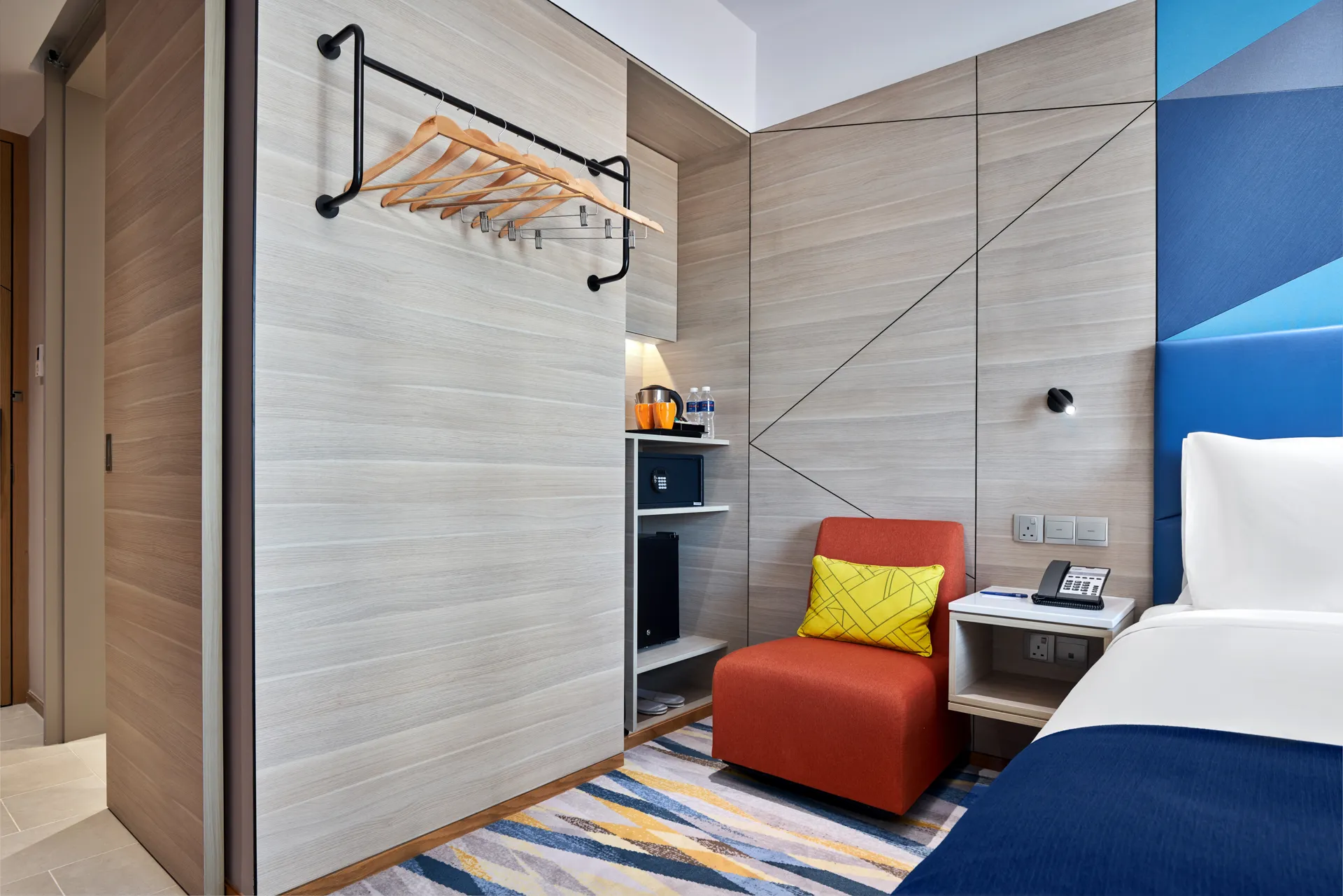 Room amenities with wardrobe rail, kettle, safe and orange accent chair — Holiday Inn Express Serangoon hotel photography