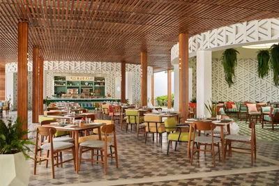 Open-air restaurant with timber-slatted ceiling, tall wooden columns, patterned tile floor, colorful mid-century chairs, and a green buffet counter at Seen Beach Club Koh Samui
