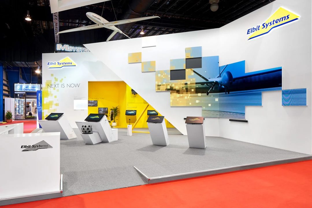 Full Elbit Systems booth with suspended UAV, digital graphics and product kiosks