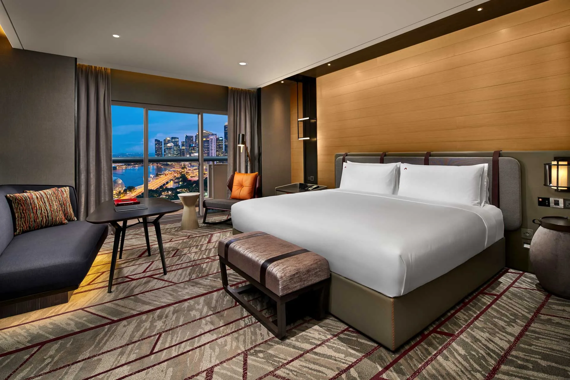 King room at night with Marina Bay skyline view, leather-strap headboard and geometric carpet