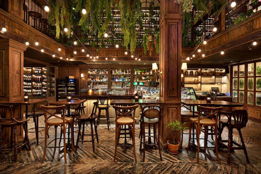 Central bar with wooden column, cross-back stools and mezzanine ferns above
