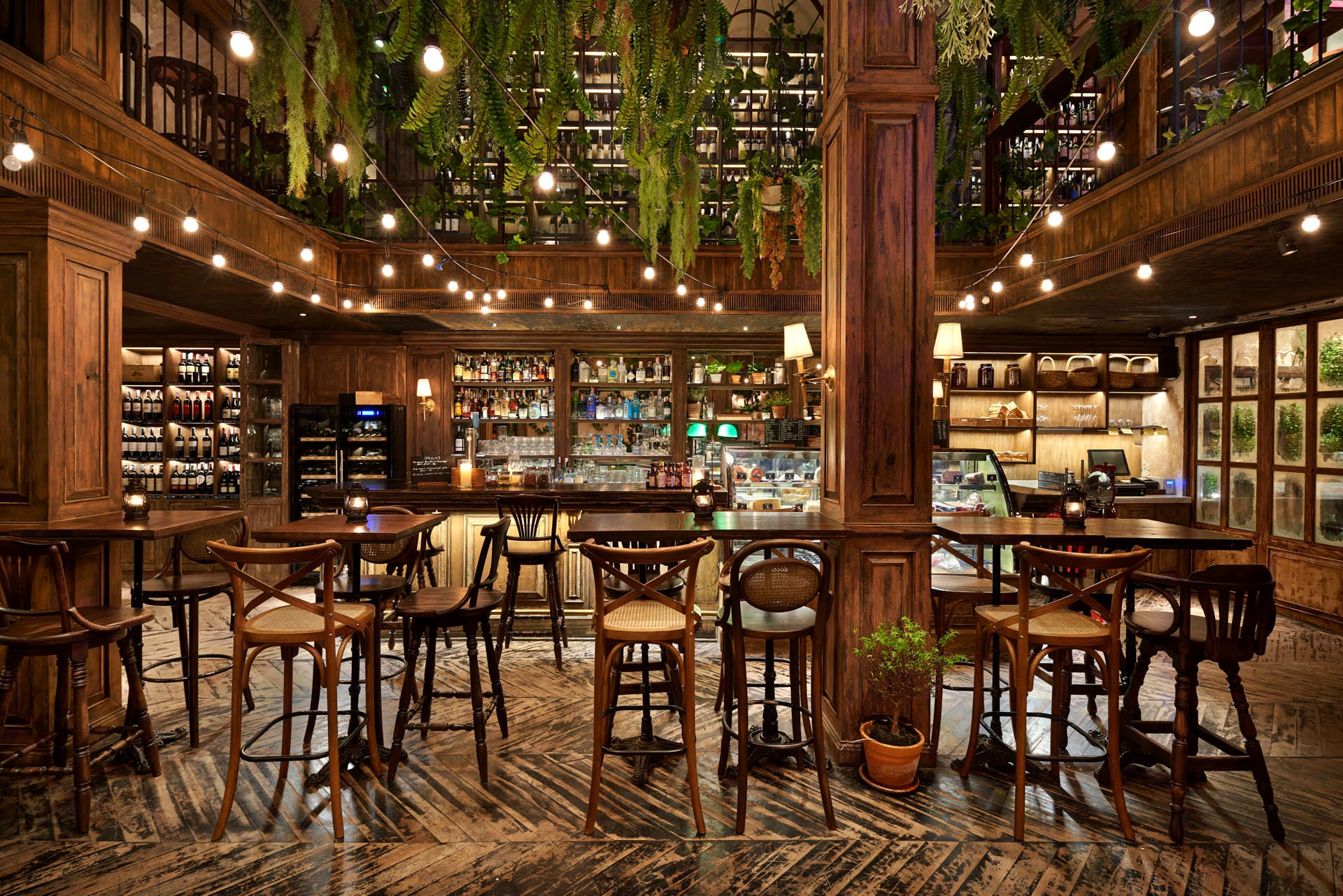 Central bar with wooden column, cross-back stools and mezzanine ferns above