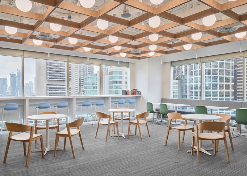 Bright office cafe area with round tables, wooden chairs and city skyline views