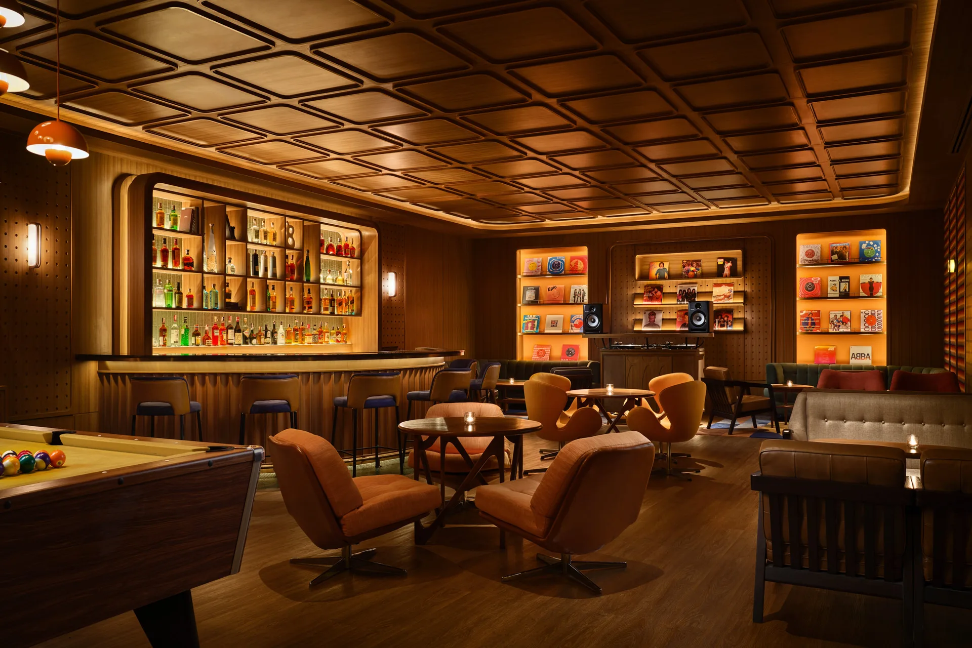 Retro lounge with wood paneling, backlit bar, pool table, swivel armchairs, and illuminated display shelves