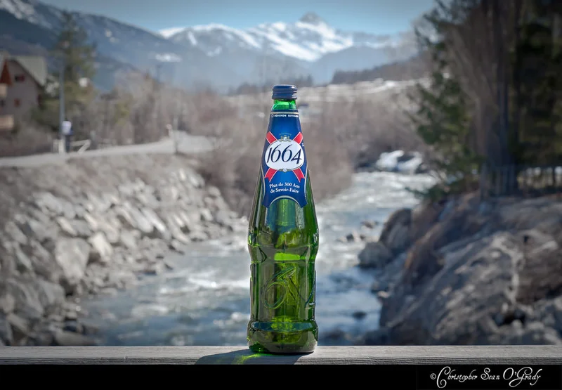 Kronenbourg 1664 bottle on a ledge with snowy French Alps and river
