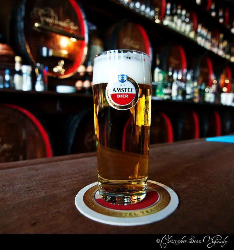 Amstel Bier draft in branded glass on a bar with wooden barrels behind