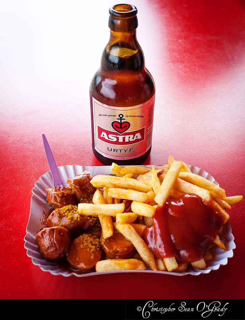 Astra Urtyp beer bottle with currywurst and fries on a red table