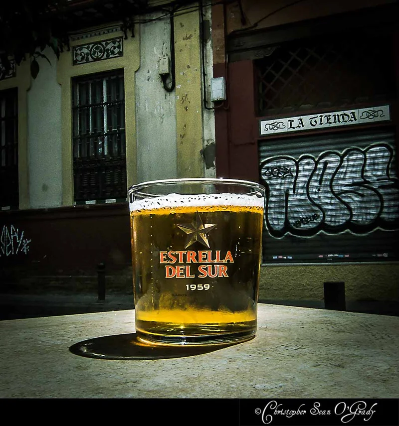 Estrella del Sur beer in branded glass at a Spanish sidewalk cafe with graffiti