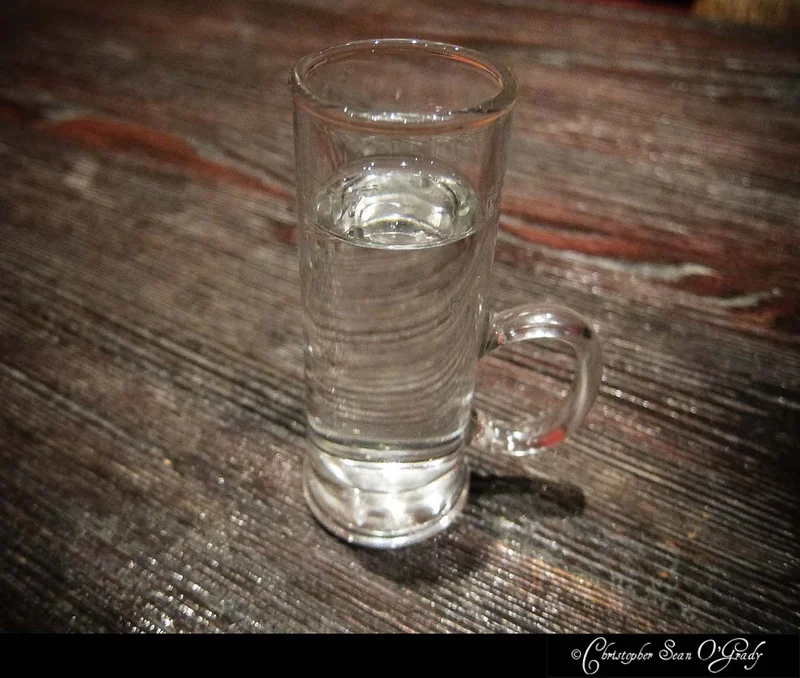 Clear spirit in a handled shot glass on a rustic wooden bar table