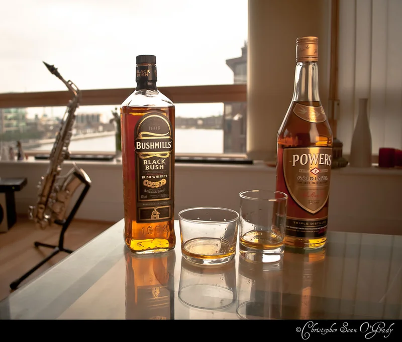Bushmills Black Bush and Powers Gold Label Irish whiskeys at sunset window