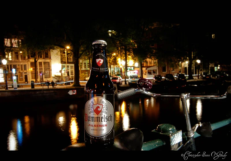 Dommelsch Pilsener bottle on a bicycle by an Amsterdam canal at night